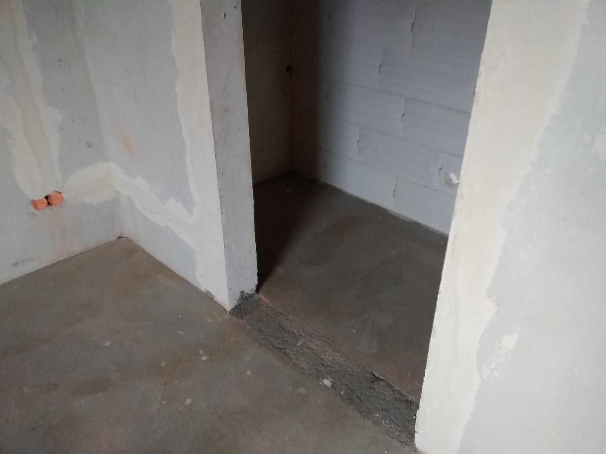 Surowy stan wnętrza po wylewce podłogi i wstępnym szpachlowaniu ścian, widoczne puszki elektryczne.