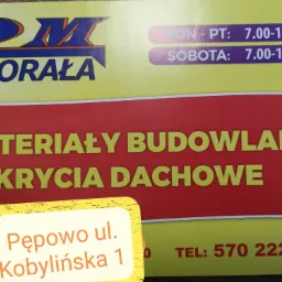 Żółto-czerwony szyld reklamowy firmy '2M Chorała' oferującej materiały budowlane i pokrycia dachowe, z podanym adresem Pępowo ul. Kobylińska 1 i numerem telefonu 570 222 902 oraz godzinami otwarcia...