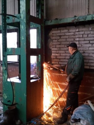 Pracownik w czapce tnie metalową konstrukcję spawarką, iskry rozbryzgują się na boki, widoczny fragment ceglanej ściany i zielona konstrukcja nośna.