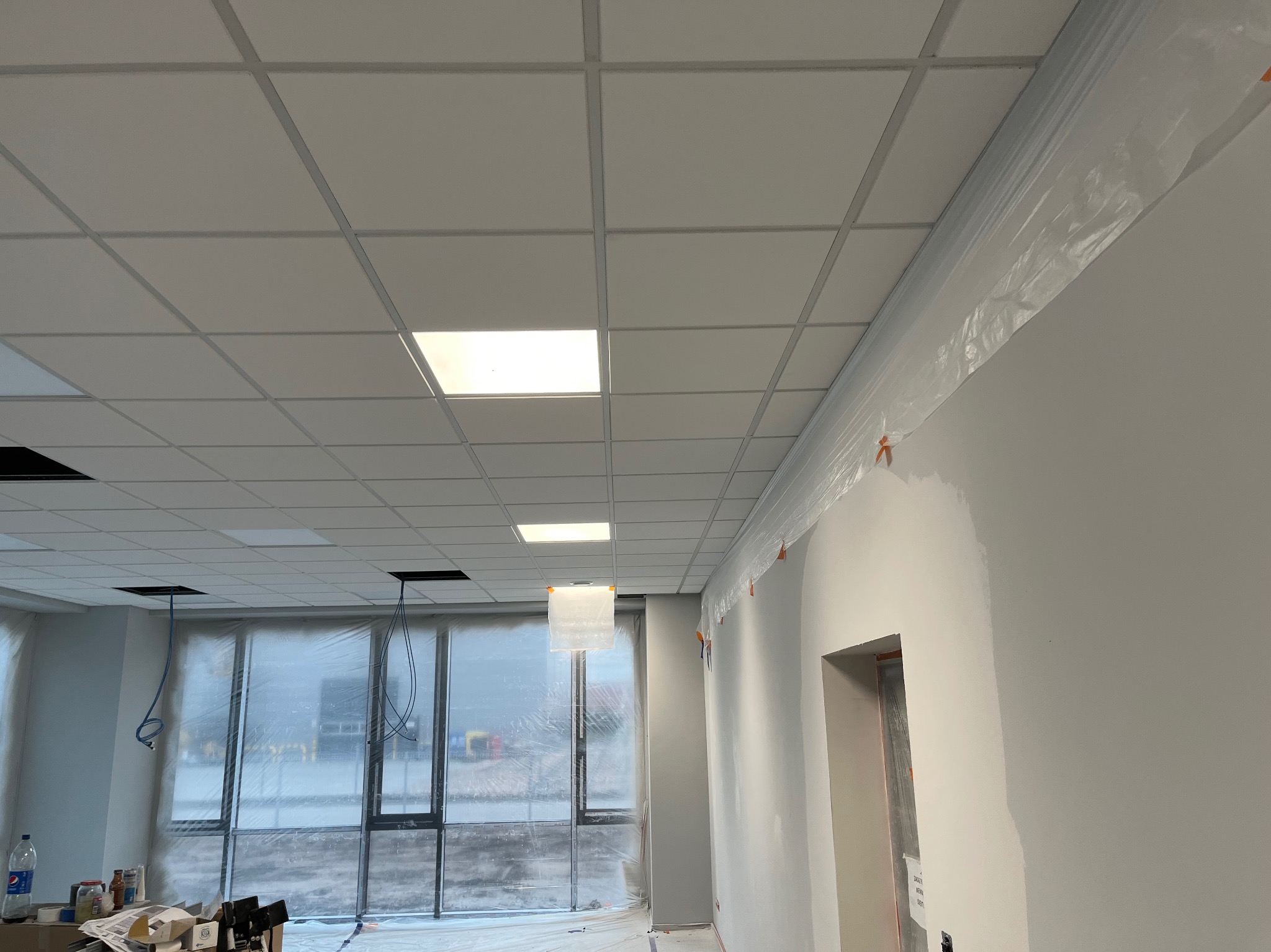 Montaż sufitu podwieszanego kasetonowego w nowym biurze, widoczne zabezpieczone folią okna i ściany, oraz wystające kable instalacji elektrycznej.
