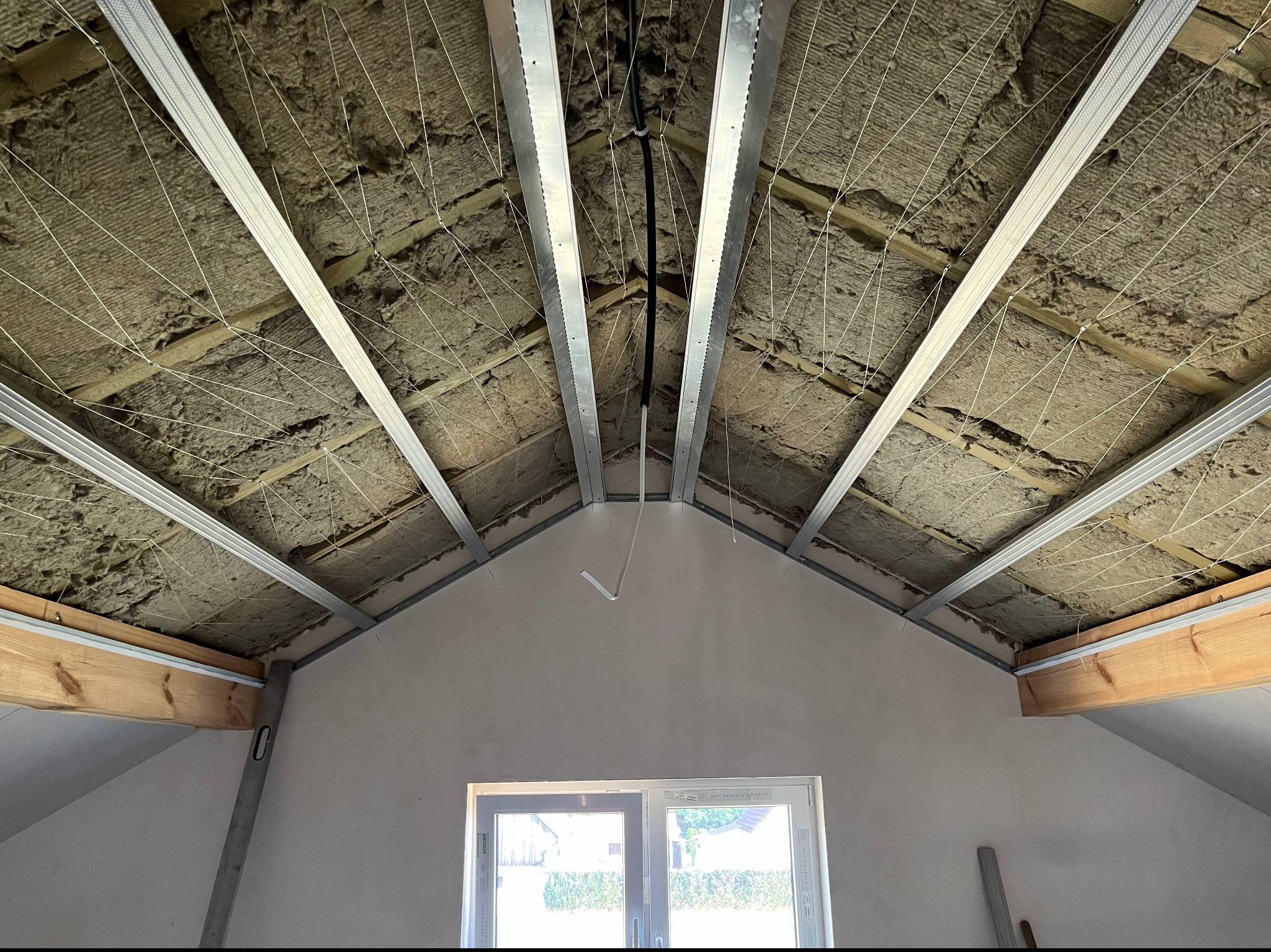 Poddasze w trakcie ocieplania: widoczne krokwie z izolacją, metalowe profile pod konstrukcję sufitu i wystające przewody elektryczne.