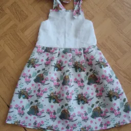 Dziewczęca sukienka z białym karczkiem i spódnicą w kwiaty i lamparty, leżąca na drewnianej podłodze.