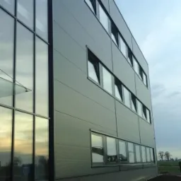 Nowoczesny budynek biurowy w Mieścisku z szarą elewacją panelową i dużymi oknami, widok z dołu na elewację i fragment chodnika.