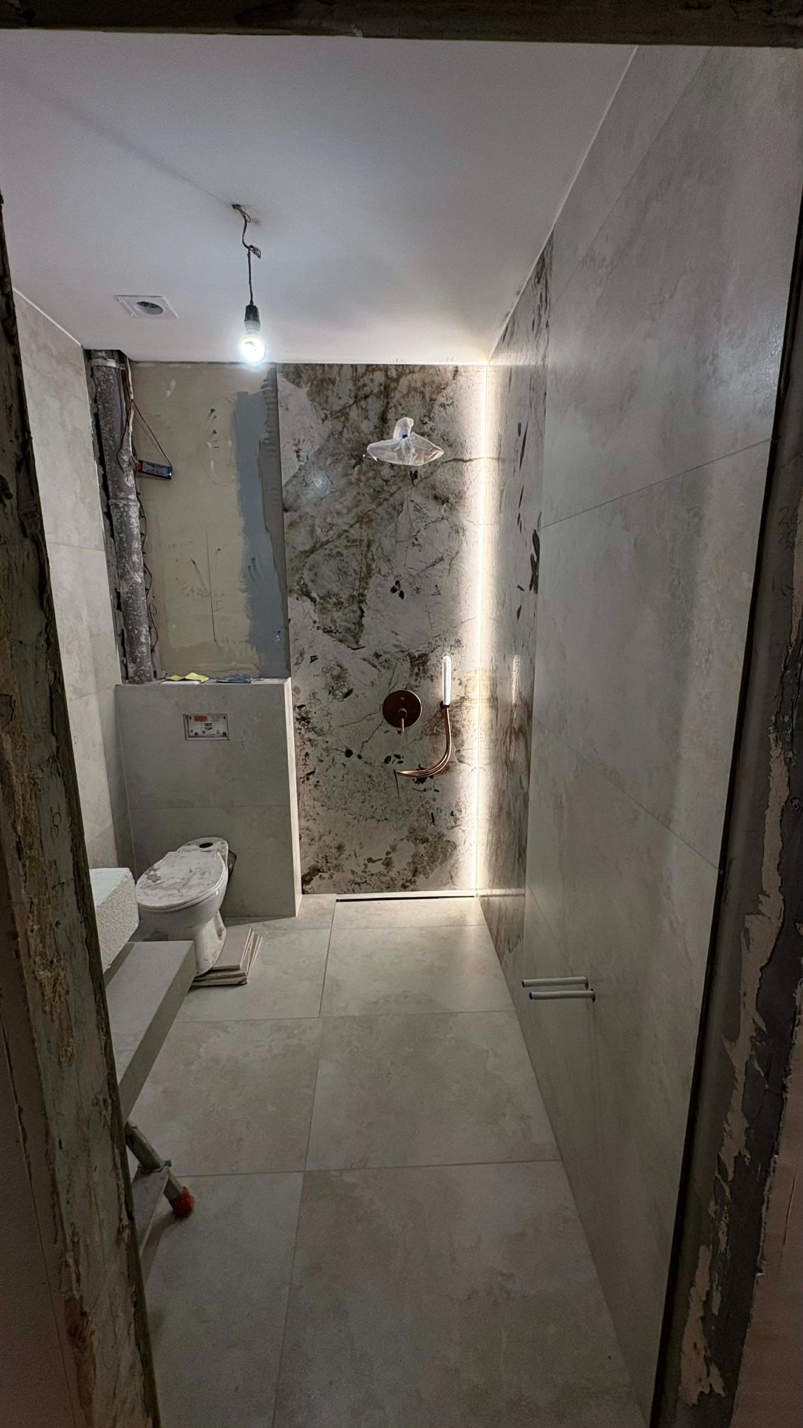 Remont łazienki w trakcie: położone płytki podłogowe i ścienne, widoczna instalacja prysznicowa z oświetleniem LED. Część ściany jeszcze w stanie surowym.