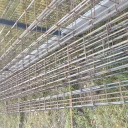 Siatka z prętów zbrojeniowych ułożona na trawie, widoczne także elementy konstrukcyjne ogrodzenia.