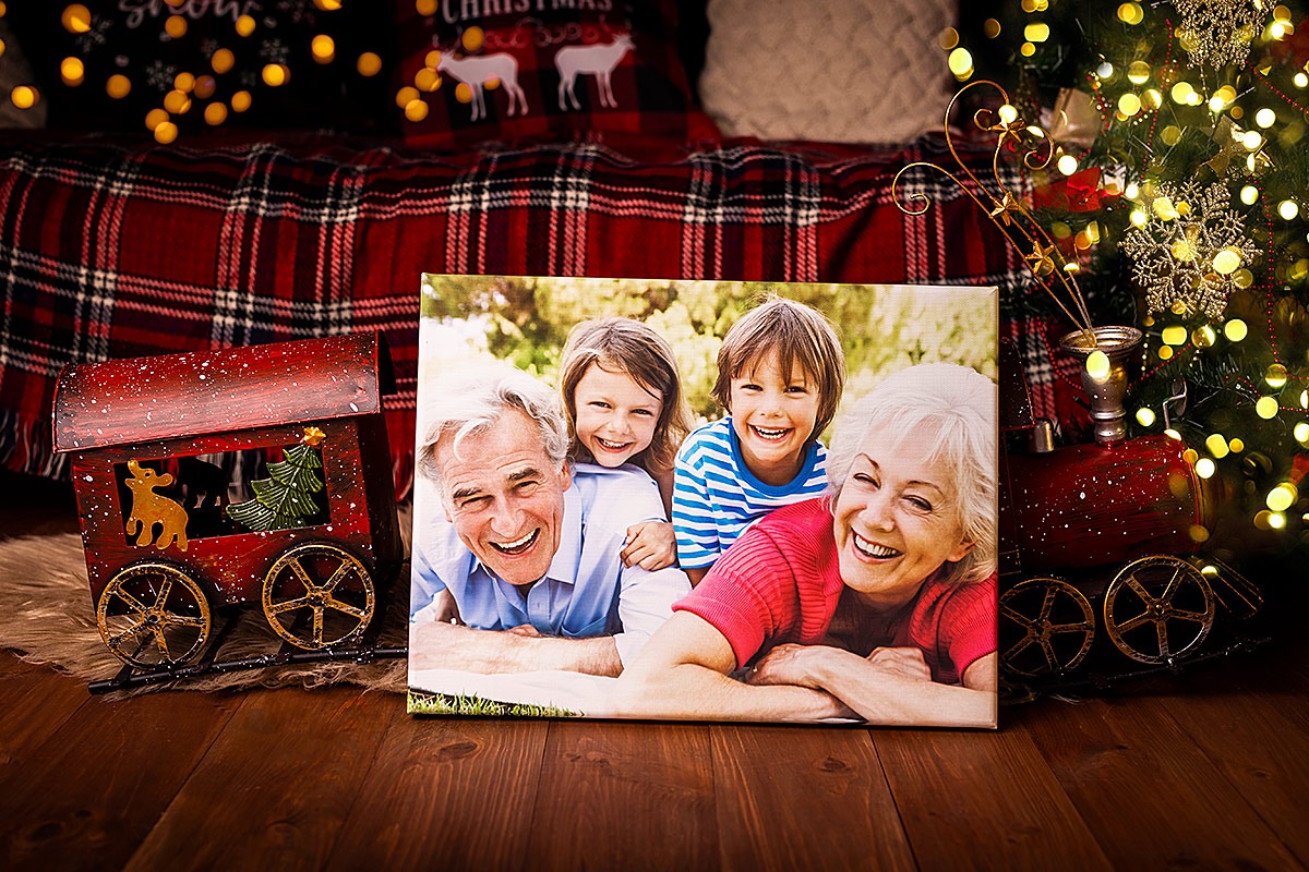 Canvas print featuring a smiling family portrait, displayed against a festive backdrop with a toy train and Christmas tree lights.