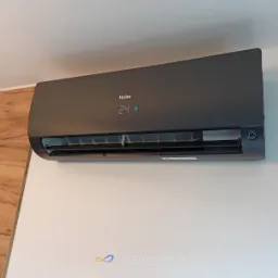 Czarny klimatyzator Haier zamontowany na białej ścianie, wyświetlający temperaturę 24 stopnie Celsjusza.