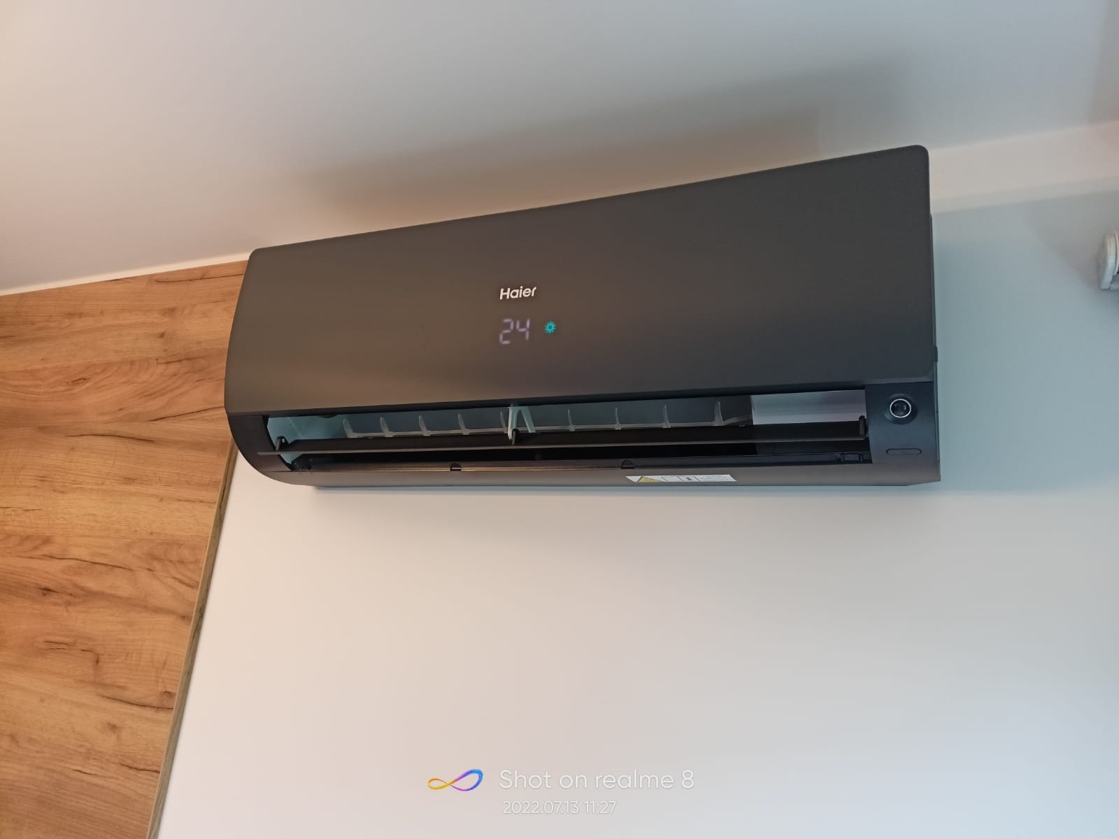Czarny klimatyzator Haier zamontowany na białej ścianie, wyświetlający temperaturę 24 stopnie Celsjusza.