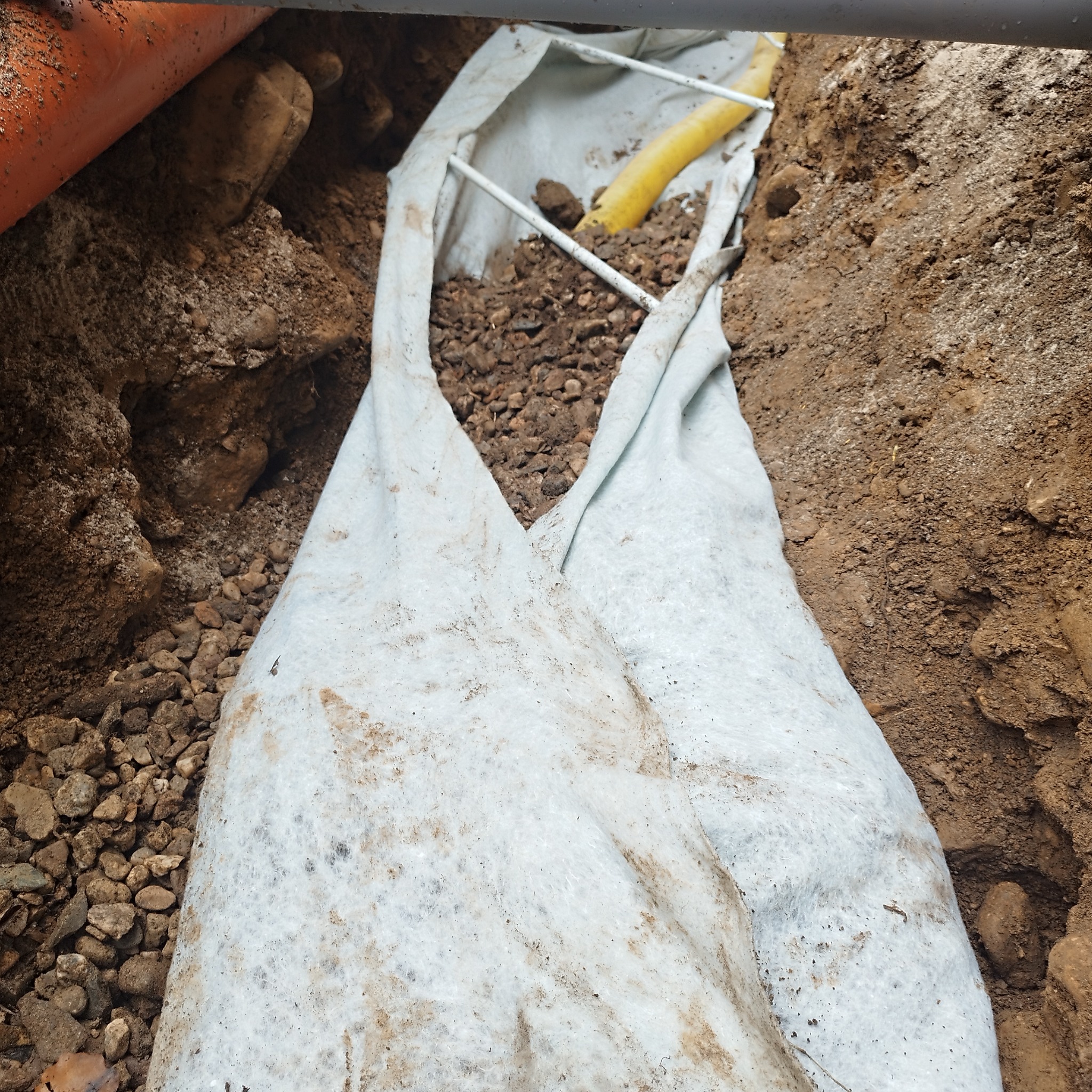 Wykop w ziemi z widoczną białą geowłókniną i żółtą rurą, zabezpieczone konstrukcją metalową, prace ziemne w Mysłakowicach.