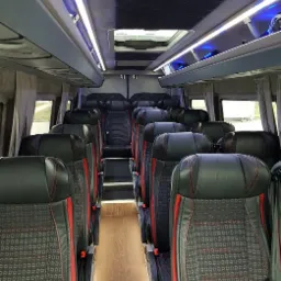 Wnętrze luksusowego busa z czarnymi skórzanymi fotelami z czerwonymi akcentami, oświetleniem LED i jasną podłogą.