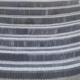 Półokrągłe schody zewnętrzne wyłożone szarą kostką brukową w dwóch odcieniach, z czarnymi obrzeżami z kostki typu piccolo.