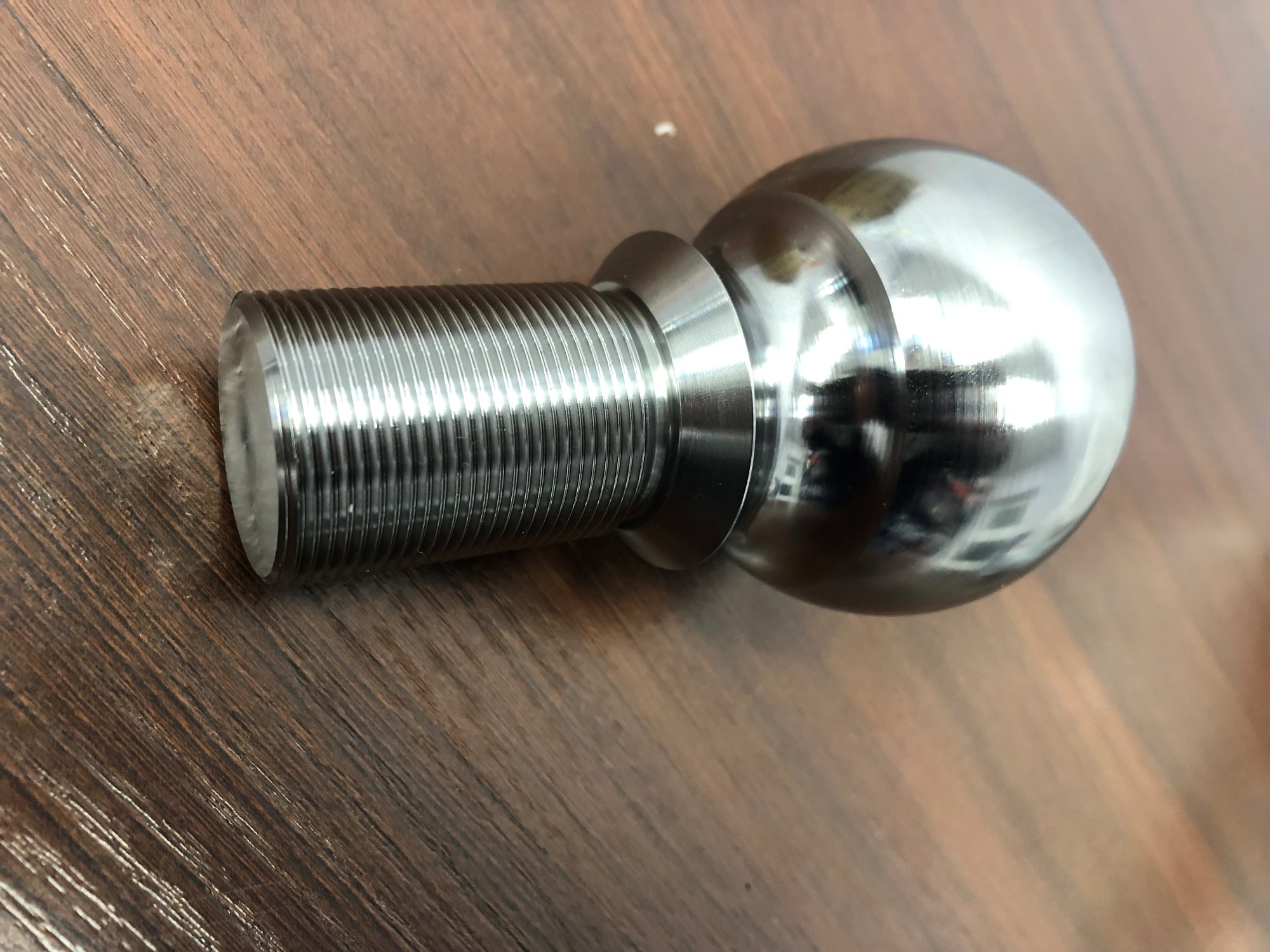 Precyzyjnie wykonany, chromowany element metalowy z gwintem i kulistym zakończeniem, leżący na drewnianej powierzchni.