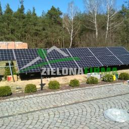 Zielonewolty.pl - Instalacja fotowoltaiczna na gruncie z widocznymi panelami, konstrukcją wsporczą, narzędziami i materiałami przygotowanymi do montażu, na tle lasu i kostki brukowej.