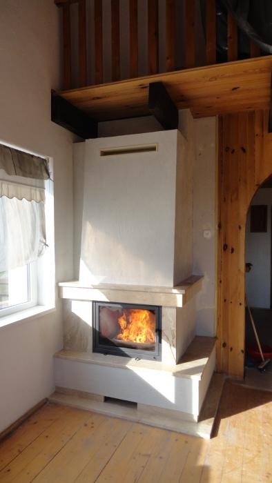 Nowoczesny, biały piec z paleniskiem i płomieniami, umieszczony w jasnym pomieszczeniu z drewnianą podłogą i elementami konstrukcyjnymi z drewna.