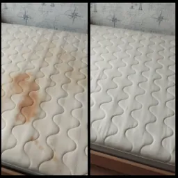 Materac z widoczną plamą przed i po czyszczeniu, ukazujący skuteczność zabiegu. Widoczny wzór pikowania materaca i tapeta w tle.