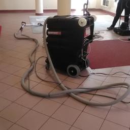 Jg pranie - Profesjonalny sprzęt do czyszczenia dywanów marki Enforcer 500 na kafelkowej podłodze w Strzelinie, w tle osoba obsługująca mniejszą maszynę czyszczącą.