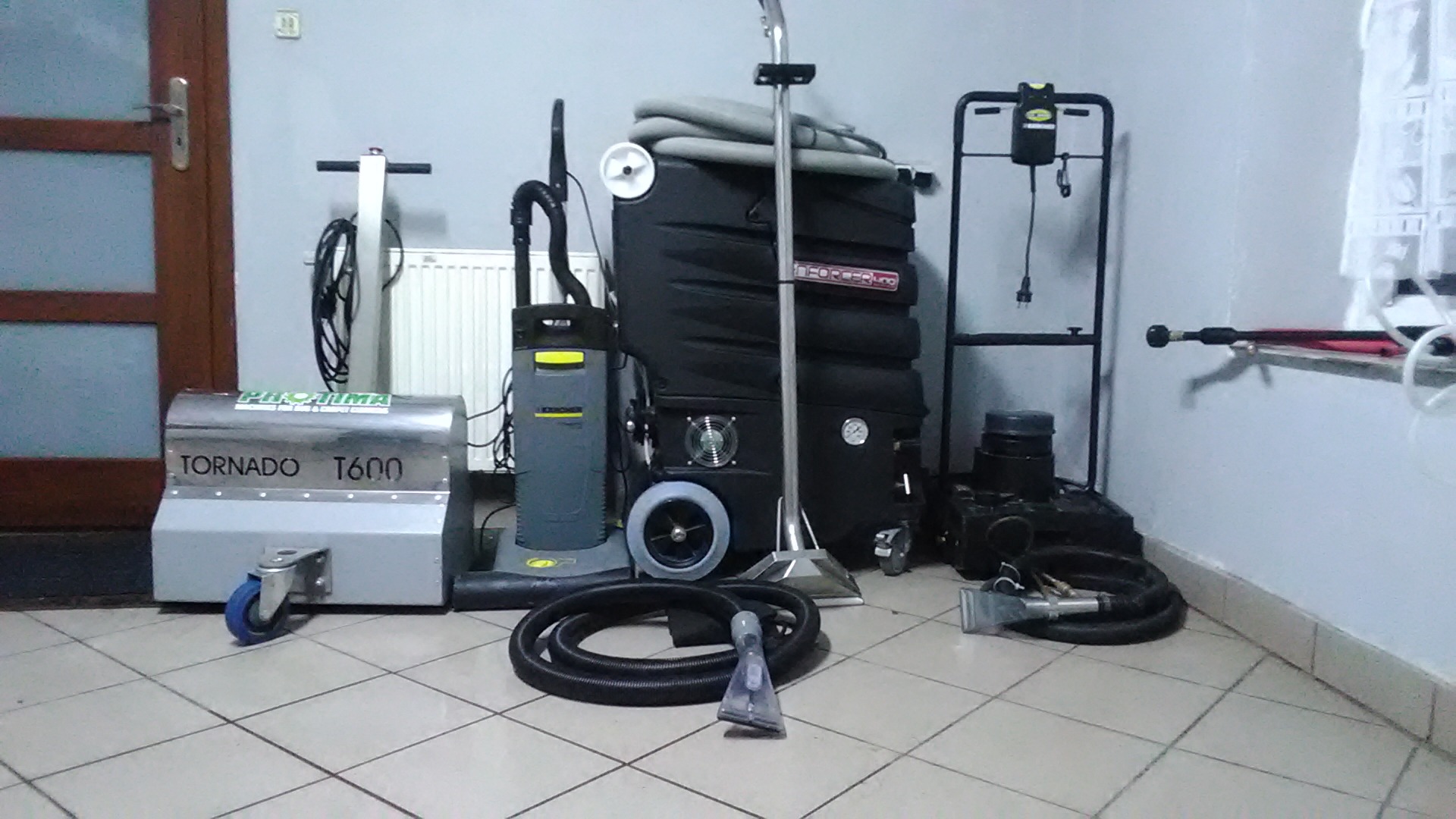 Profesjonalny sprzęt do czyszczenia tapicerki i dywanów: ekstraktor Tornado T600, odkurzacz piorący Karcher oraz duży agregat z wężami i dyszami, ustawione na kafelkach w pomieszczeniu.