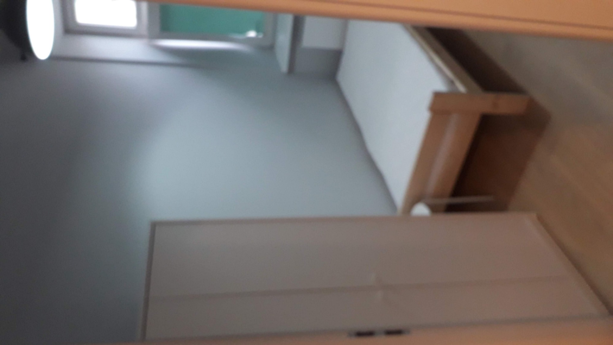 Pomalowane na szaro ściany pokoju z widoczną szafą z białymi drzwiami i łóżkiem z jasnego drewna, ujęcie z góry.