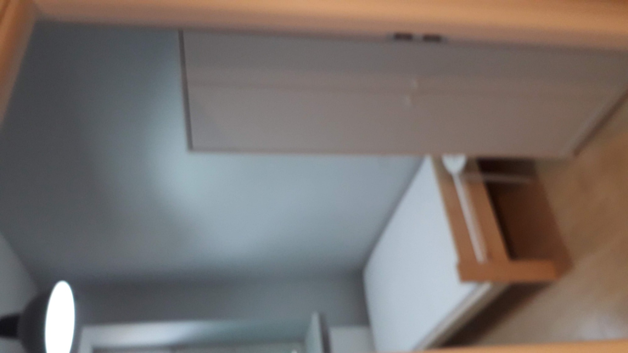 Fragment pokoju z białą szafką wiszącą i lampką biurkową w rogu, widok z dołu, rozmyte zdjęcie.