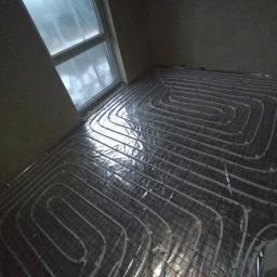 Żywioły Sp. z o.o. - Układ rur ogrzewania podłogowego na siatce montażowej, widok z góry w rogu pomieszczenia z oknem, przygotowane do zalania wylewką.