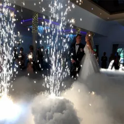 Para młoda tańczy w chmurze dymu, otoczona fontannami iskier podczas wesela.