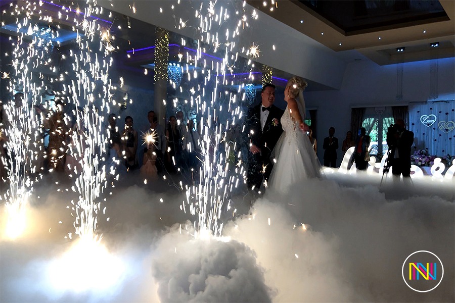Para młoda tańczy w chmurze dymu, otoczona fontannami iskier podczas wesela.