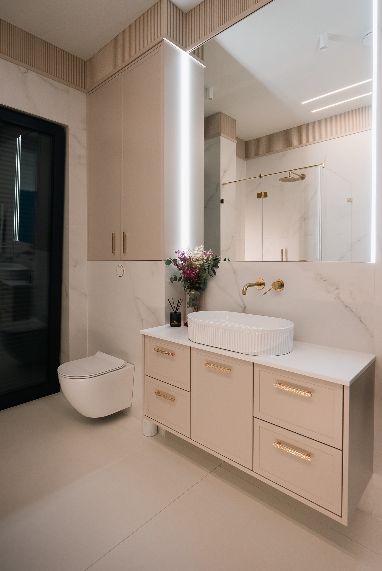 Elegancka łazienka z beżowymi szafkami na wymiar i umywalką w Debrznie. Lustro z podświetleniem LED, złote akcenty i marmurowe wykończenie tworzą luksusowy wygląd.