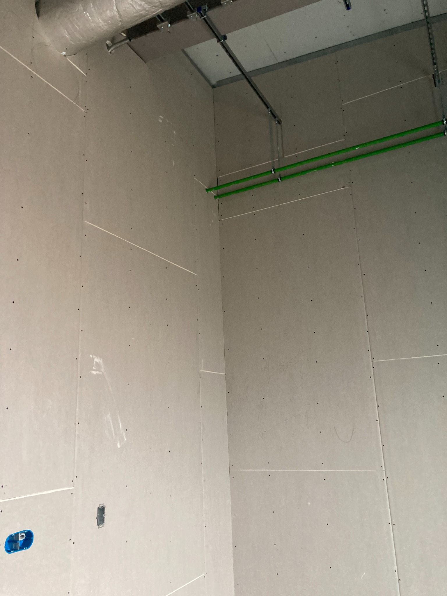 Wnętrze w trakcie montażu płyt kartonowo-gipsowych, widoczne zielone rury instalacyjne pod sufitem i puszka elektryczna w ścianie.