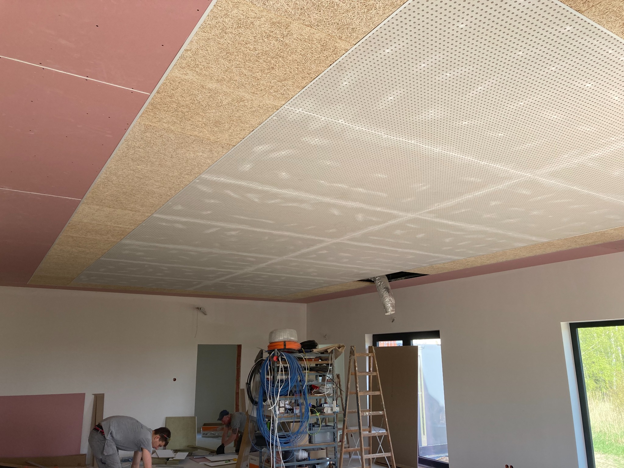 Montaż sufitu podwieszanego z perforowanej płyty w pomieszczeniu, widoczny pracownik i drabina z narzędziami.