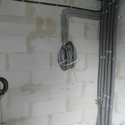 Kable elektryczne w peszlach i bez, poprowadzone po ścianie z betonu komórkowego, widoczne uchwyty mocujące.