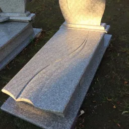 Szary, granitowy pomnik z wygrawerowanym motywem roślinnym, ustawiony na trawniku w słoneczny dzień.