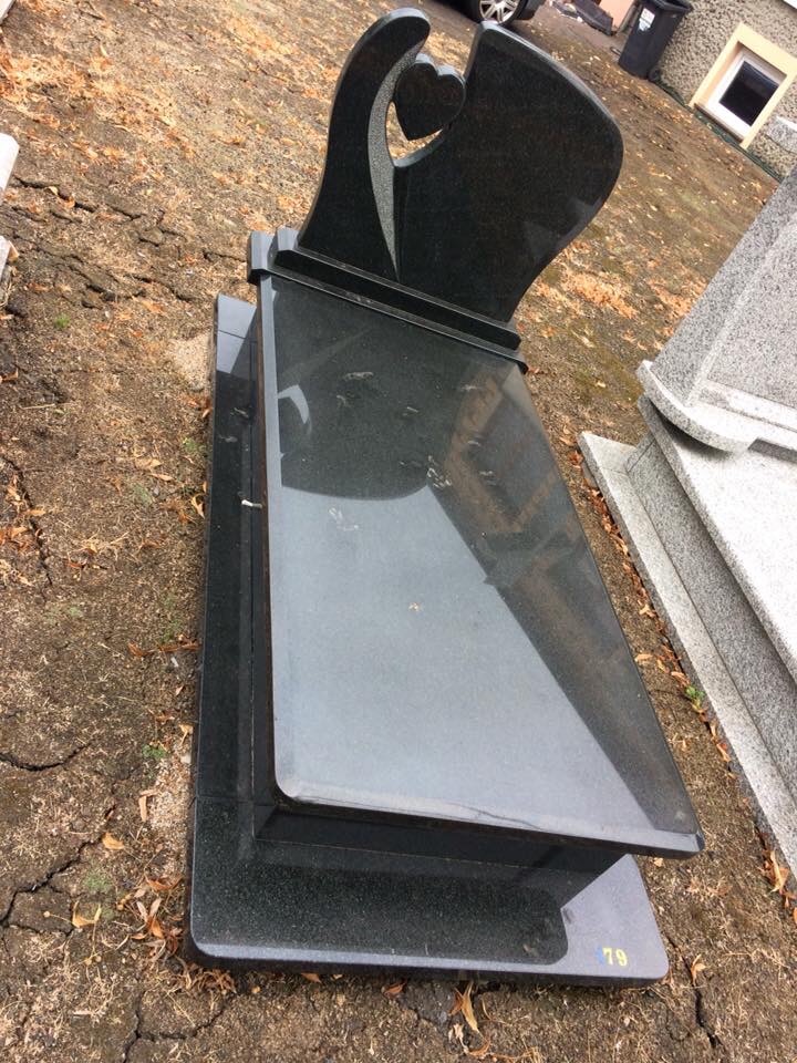 Nowoczesny, czarny pomnik z motywem serca, ustawiony na żwirowym podłożu, z widocznym numerem '79' w dolnym rogu.