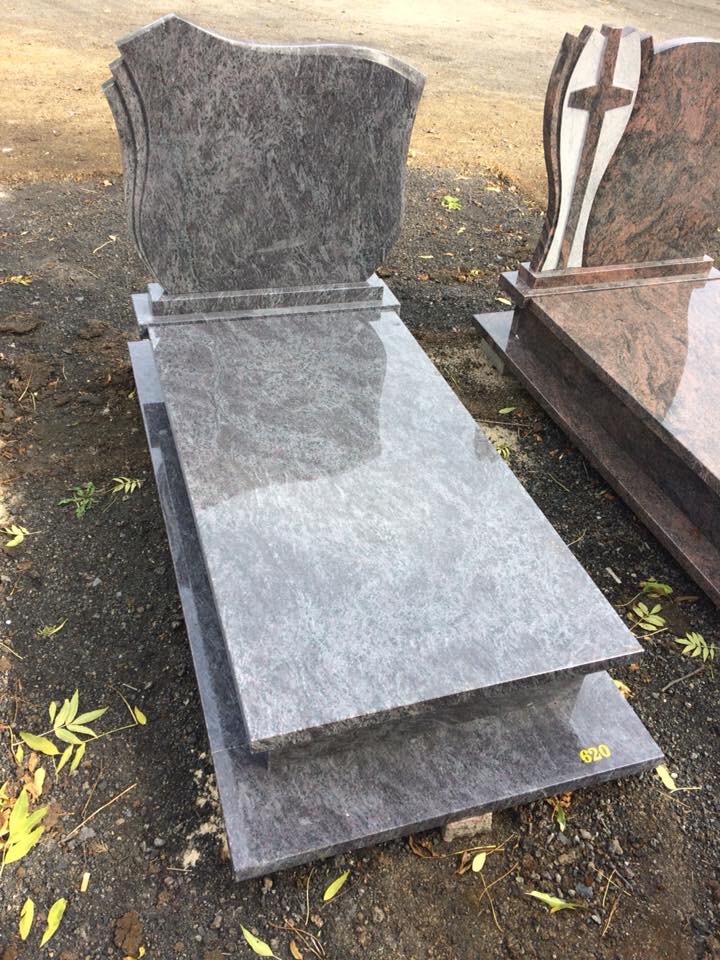 Szary, granitowy pomnik z falistym wykończeniem nagrobka, ustawiony na ziemi z liśćmi, z widocznym numerem '620' w prawym dolnym rogu.