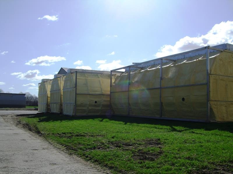 Szkielety konstrukcji z wypełnieniem izolacyjnym w kolorze żółtym, ustawione szeregowo na trawiastym terenie, widoczne na tle błękitnego nieba z chmurami.