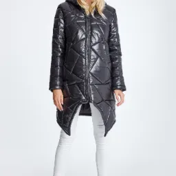 Modelka prezentuje błyszczącą, pikowaną kurtkę z asymetrycznym dołem, w połączeniu z białymi spodniami i butami w stylu rockowym na białym tle.