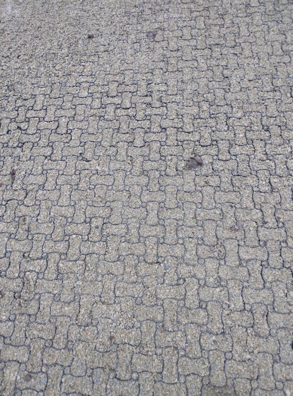 Szara, przepuszczalna nawierzchnia z plastikowej siatki wypełnionej drobnym żwirem, widoczna z góry.