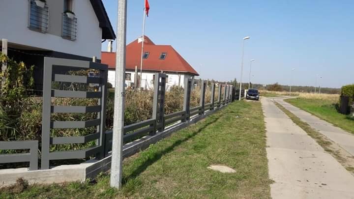 Nowoczesne ogrodzenie panelowe w kolorze szarym, z poziomymi przęsłami, oddzielające posesję od drogi dojazdowej.