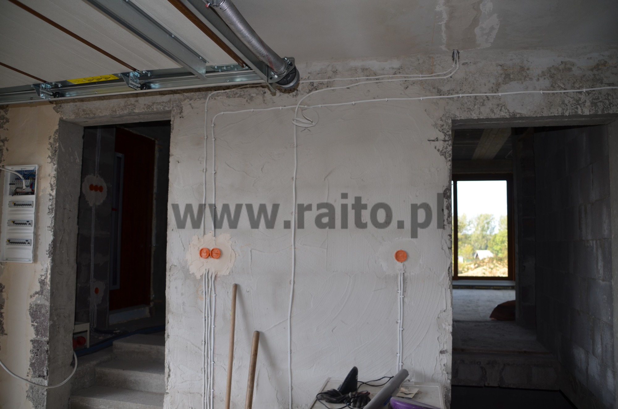 Wnętrze w stanie surowym z widocznymi przewodami elektrycznymi w ścianach, puszkami instalacyjnymi i narzędziami na podłodze, instalacja podtynkowo.