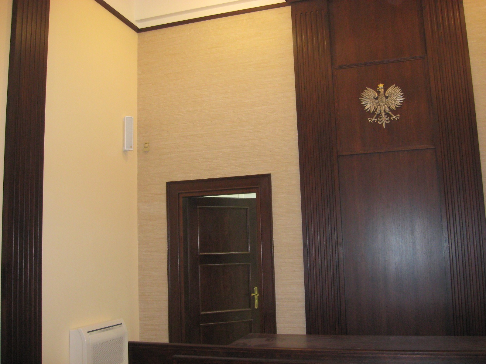 Eleganckie wykończenie wnętrza sali sądowej w Białymstoku, z drewnianą boazerią, godłem Polski i beżową tapetą.