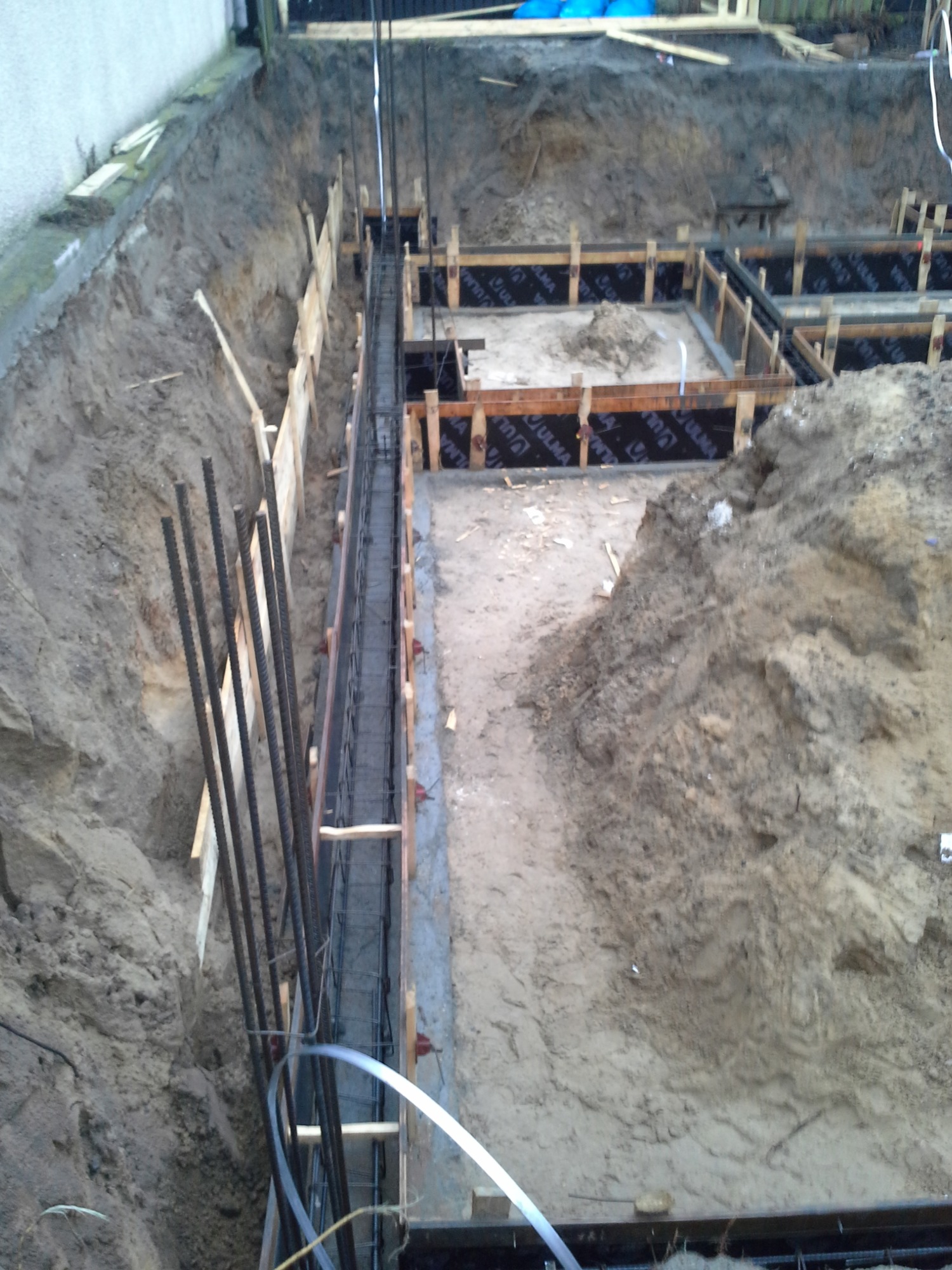 Wykonanie fundamentów: wykop z drewnianym szalunkiem, zbrojenie stalowe pionowe i poziome, izolacja przeciwwilgociowa na podłożu.