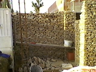 Wznoszenie kamiennej ściany z nieregularnych, płaskich kamieni, widoczne rusztowanie i narzędzia murarskie, częściowo ukończona konstrukcja.