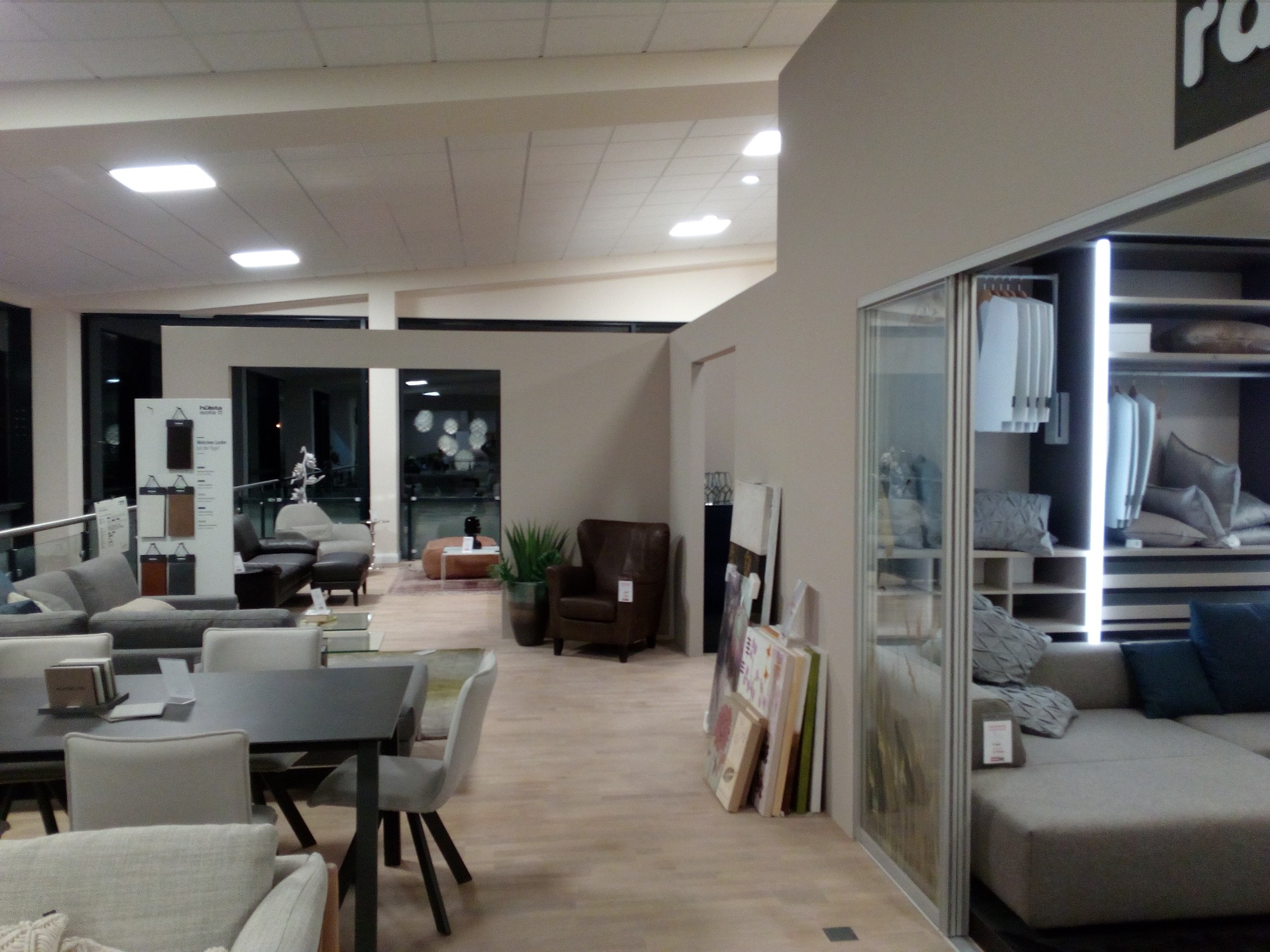 Salon meblowy z ekspozycją sof, stołów i krzeseł, oświetlony panelami sufitowymi, z widoczną aranżacją wnętrza.