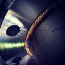 Spoina na okrągłym elemencie metalowym z widocznymi otworami, ukazująca charakterystyczne zabarwienie po procesie łączenia metali.