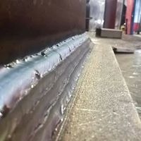 Spoina pachwinowa łącząca dwie stalowe konstrukcje, widoczne ślady termiczne i drobne odpryski, szary beton w tle.