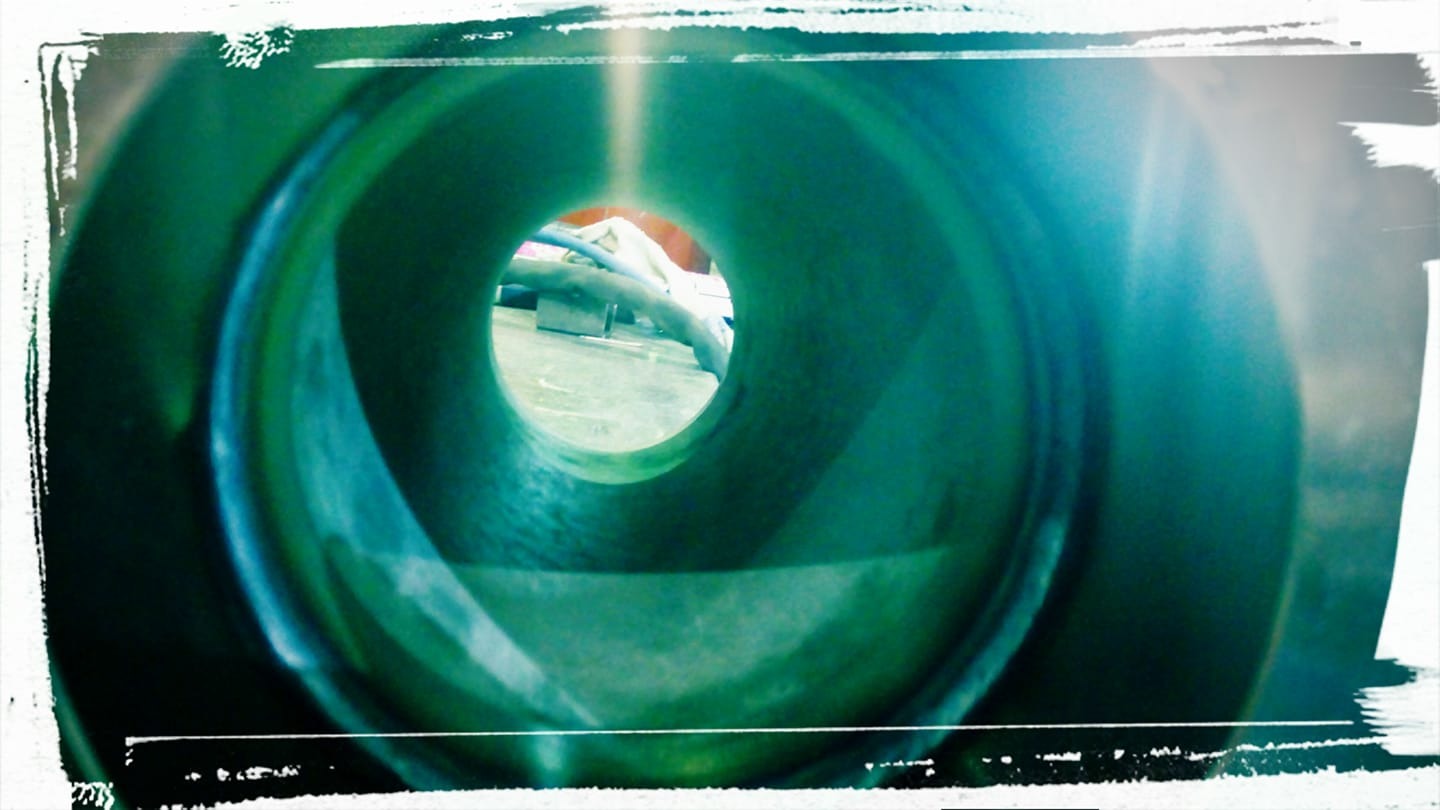 Wnętrze metalowej rury o zielonkawym odcieniu, widok z bliska na spawany szew i elementy konstrukcyjne w tle.