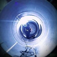 Spawanie wewnętrzne rurociągu, widok z wnętrza rury, iskrzące się światło spawarki, przewody spawalnicze w tle.