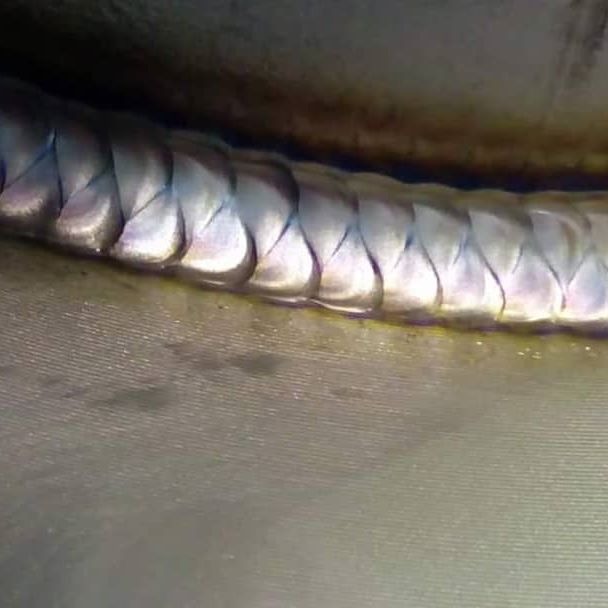 Zbliżenie na estetyczne spawy układające się w regularny wzór, z widocznymi tęczowymi przebarwieniami termicznymi.