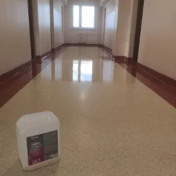 Błyszcząca, świeżo umyta podłoga w korytarzu budynku z terazzo, obok biały kanister z płynem czyszczącym Clindex HARD.