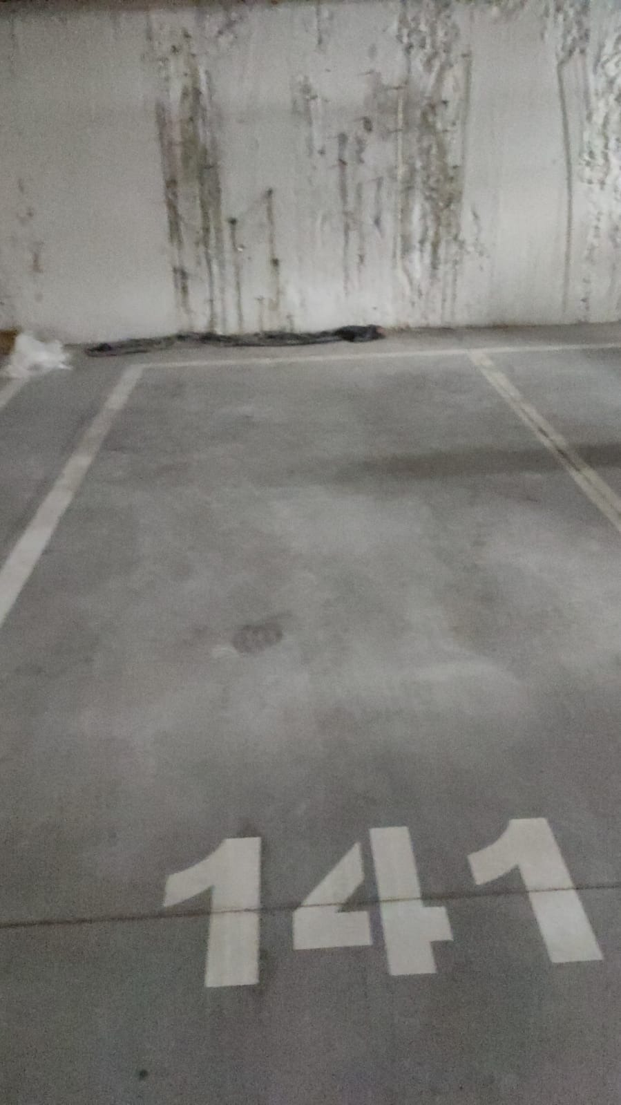 Szara betonowa posadzka parkingu podziemnego z numerem stanowiska 141, ściana z zaciekami i śladami wilgoci.