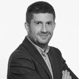 Portret biznesowy mężczyzny w ciemnej marynarce i jasnej koszuli, czarno-biały, na białym tle.